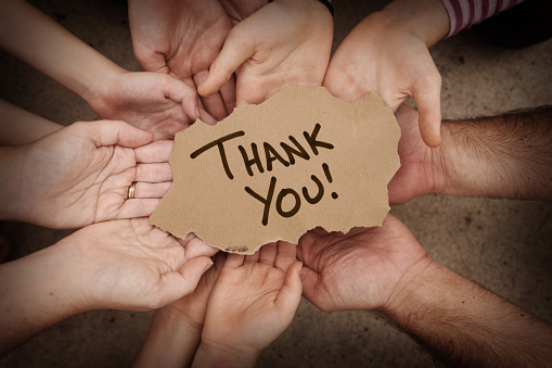 Thank You written on cardboard being held in hands by a group of people.  Stock image of a lot of hands holding torn cardboard.