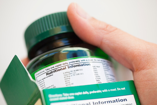 Human hand take out bottle with vitamin pills from the box for reading Nutritional information.