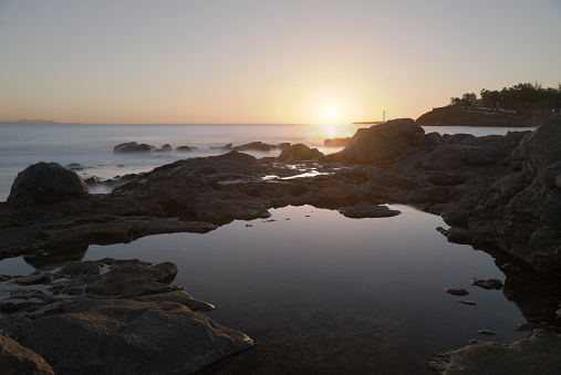 A high dynamic range landscape of rockpools at sunset in Playa Blanca, Lanzarote, with the Faro de Pechiguera Lighthouse in the background.