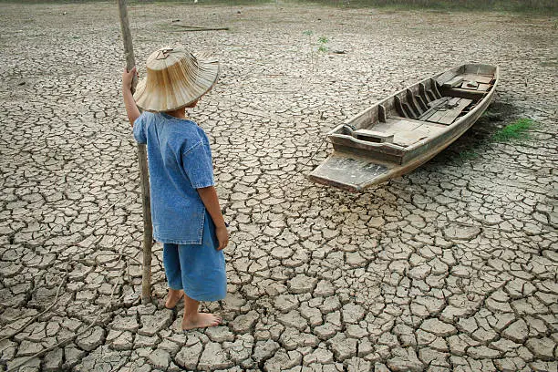 Children standing near the wooden boat on cracked earth. Metaphor for Global warming and Climate change.