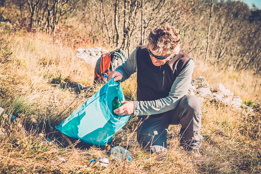 Man collecting garbage into plastic bag in nature