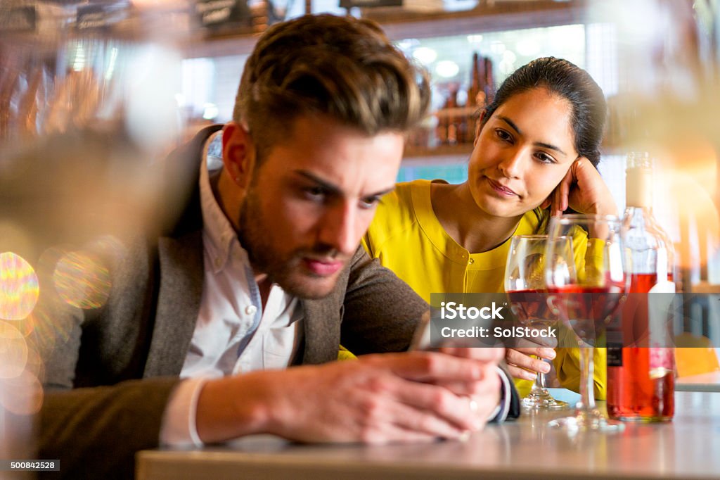 Rude Behaviour A couple are out having drinks and the woman looks irritated that her partner is on his mobile phone and not paying her any attention. Rudeness Stock Photo