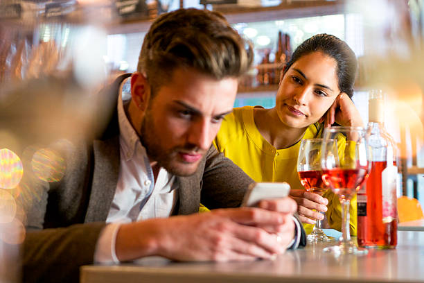 Rude Behaviour A couple are out having drinks and the woman looks irritated that her partner is on his mobile phone and not paying her any attention. couple on bad date stock pictures, royalty-free photos & images