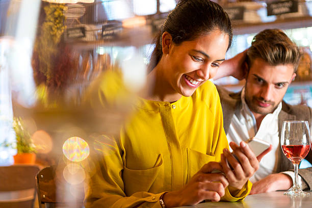 Rude Behaviour A couple are out having drinks and the man looks irritated that his partner seems more interested in texting on her mobile phone than paying him any attention. vex nightclub stock pictures, royalty-free photos & images