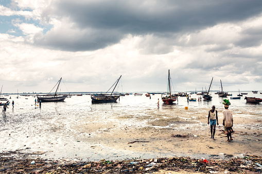 Zanzibar, Tanzania - September 6, 2015: Fishermen boats with local people in lively fishing village Mkokotoni (Zanzibar island). The place is full of garbage and it is used by local vessels and fishing boats for selling sea food in the near fish market.