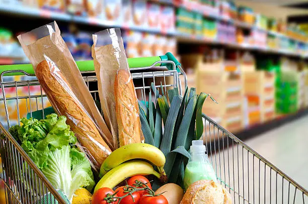 Shopping cart full of food in the supermarket aisle. High internal view. Horizontal composition