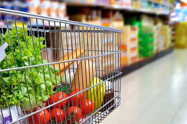 Photo of Shopping cart full of food in supermarket aisle side tilt