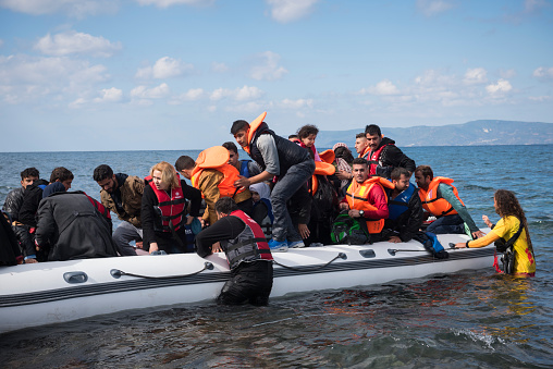 Lesbos, Greece- October 25, 2015: A volunteer lifeguard assists migrants out of their boat after they landed on the Greek island of Lesbos, near the town of Skala Sikamineas. The coastline of Turkey is visible on the right side of the photo.