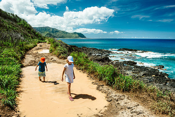 Wanderlust Hawaii Two kids crossing a big muddy puddle at Ka'ena State Park in Oahu. Hawaii. oahu stock pictures, royalty-free photos & images