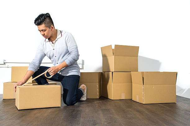 Young asian man moving house Packing cardboard using adhesive stock photo