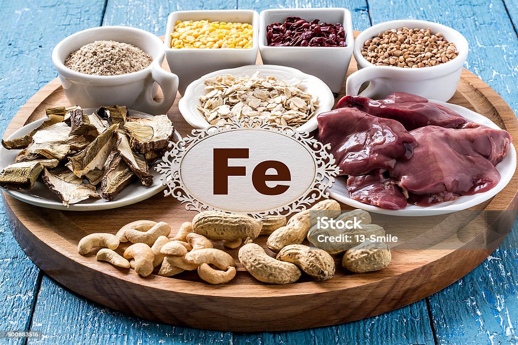 Products containing ferrum (Fe) Products containing ferrum (dried mushrooms, bran, buckwheat, livers, dogwood, cashews, oats, lentils, peanuts) on a round cutting board and a blue wooden background Assistance Stock Photo