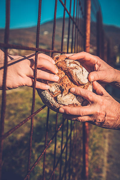 Person gives an immigrant a loaf of bread through the fence, border, hands only