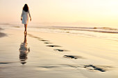 Woman leaving footprints while walking on wet sand at sunset