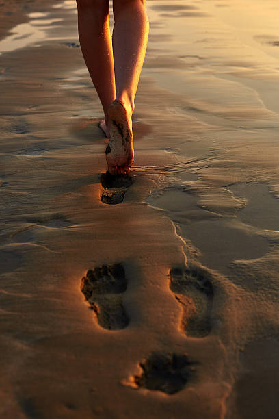 istock Woman walking barefoot on wet shore leaving footprints in sand 500907176