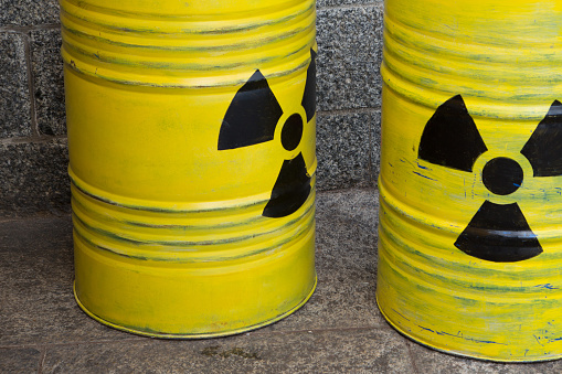 A photograph of two radioactive yellow barrels with a stone wall in the background.