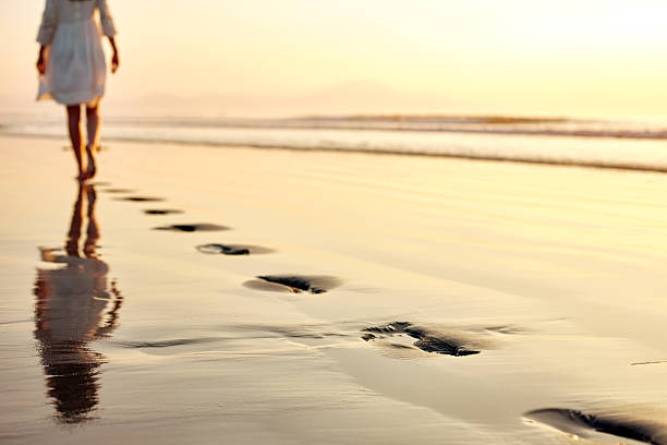 istock Footprints in wet sand with woman walking at sunset 500908808