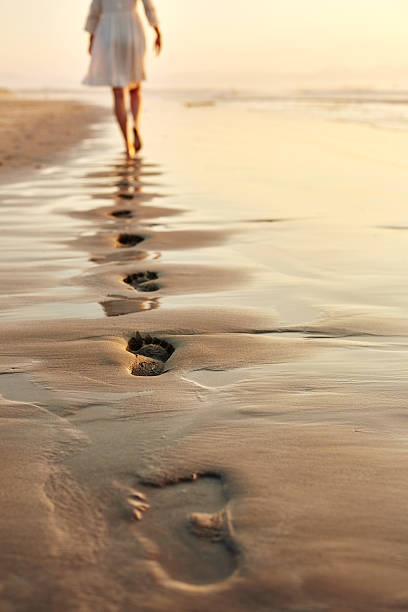 istock Woman walking barefoot on wet shore leaving footprints in sand 500910214