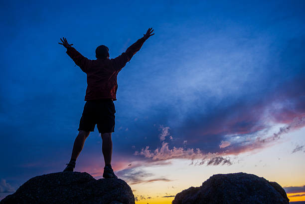 istock silhouette man arms raised into sunset sky landscape 500922955