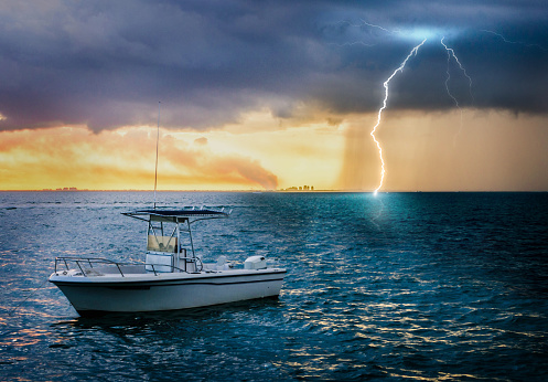 A boat floating alone in the ocean with stormy weather with lightning at sunset background. Key Biscayne, South Florida, USA.