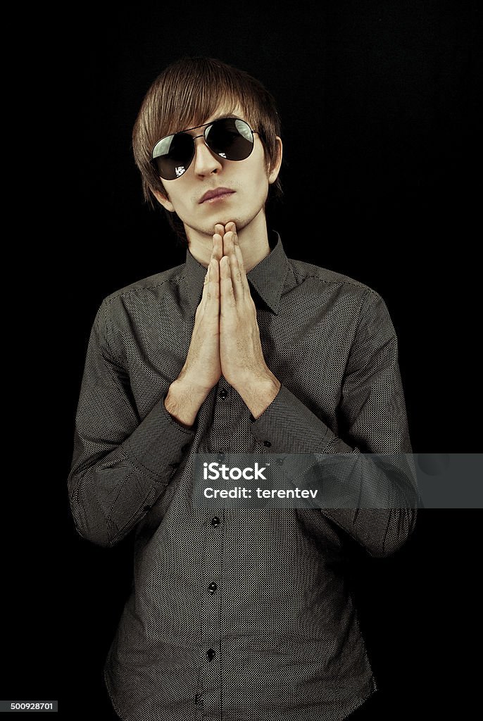 I apologize guy on a black background. prays or apologizes. it is dressed in a shirt and black glasses Adult Stock Photo