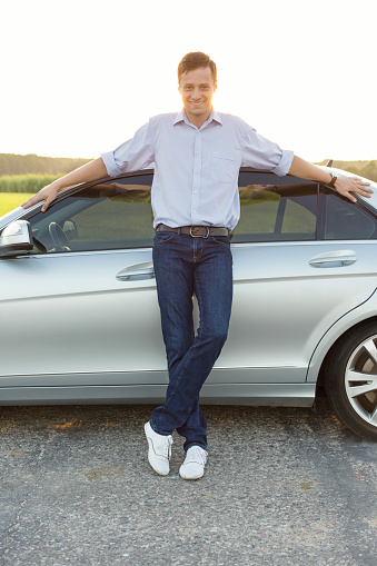Full length portrait of smiling young man leaning on car at countryside