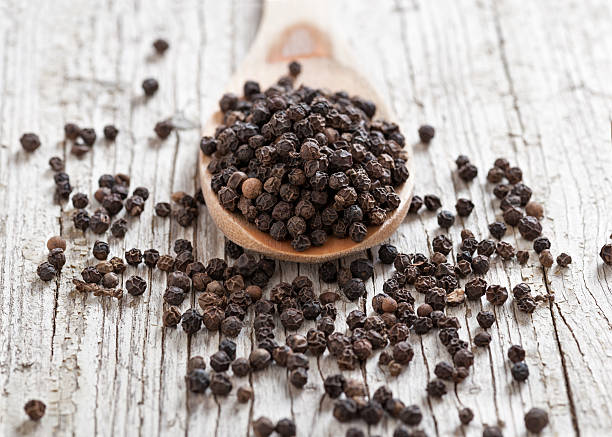 Black pepper wooden spoon with peppercorns on rustic foreground and background black peppercorn stock pictures, royalty-free photos & images