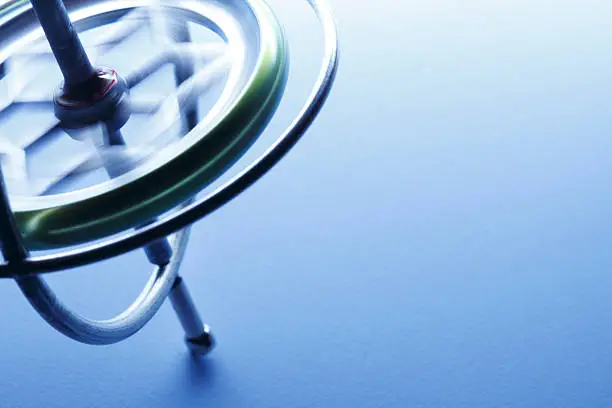 A spinning gyroscope balances on a light blue background. The gyroscope is placed to the left side of the images allowing for copy on the right. Image can be flipped horizontal to accommodate alternative compositional needs.   Shot with shallow depth of field.