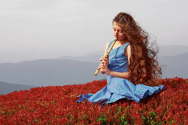 Young woman playing the flute in autumn mountains