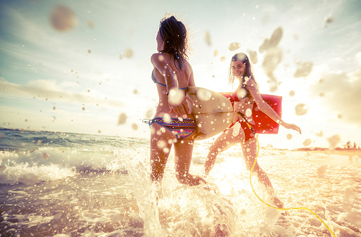 Two ladies running into the sea with surf boards