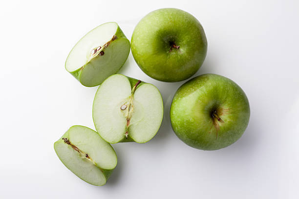 Whole and sliced green apples from above on white Two whole green apples and one sliced on white background directly from above green apple slice overhead stock pictures, royalty-free photos & images