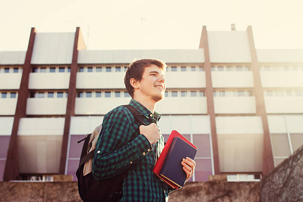 istock University.Smiling student holding a book and a bag 500965392