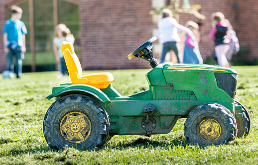 A toy tractor on a farm playground with children playing in the background