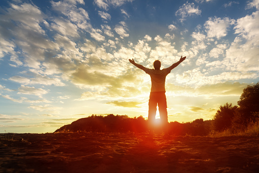 Silhouette of a man with hands raised in the sunset concept for religion, worship, prayer and praise