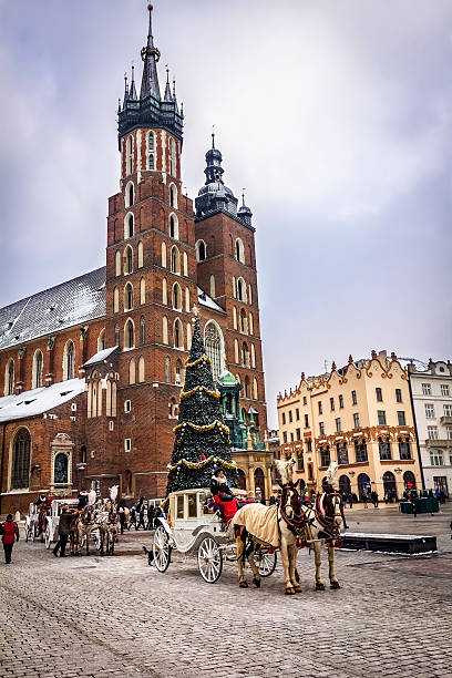 Cracow, Poland - December 27, 2014: The Main Market Square of Krakow with the church Assumption of the Blessed Virgin Mary, Christmas Tree and horse carriages, Poland