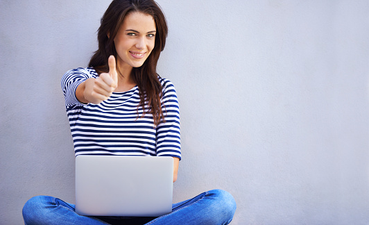 An attractive young woman showing the thumbs up sign while sitting with her laptophttp://195.154.178.81/DATA/i_collage/pi/shoots/783649.jpg