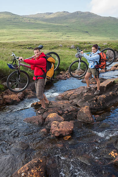 istock Couple crossing a stream holding their mountain bikes 501047069