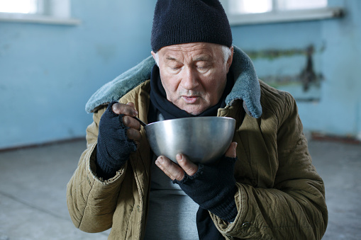 Eating man. Senior-aged tramp eating from his old iron bowl sadly.