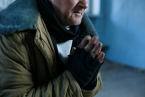 Desperate man. Old-aged beggar is sitting and holding his hands in praying gesture. 