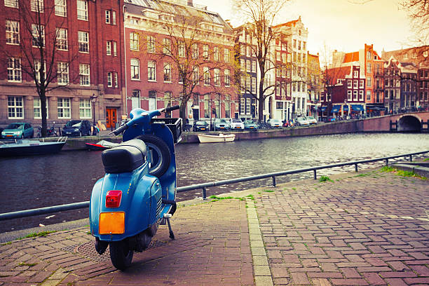 Blue scooter stands parked on the canal coast in Amsterdam. Toned effect