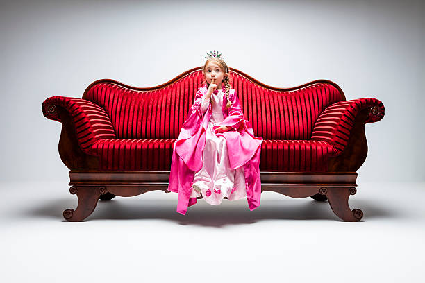 A little girl in red clothes have fun in the artificial snow by the fireplace in the studio. The girl is holding a box with gifts. A little kid in red christmas costume having fun beside a decorated christmas tree. A girl playing with falling artificial snow flakes near a christmas tree. A kid playing with artificial snow flakes falling near a christmas tree. Christmas concept. High quality photo.