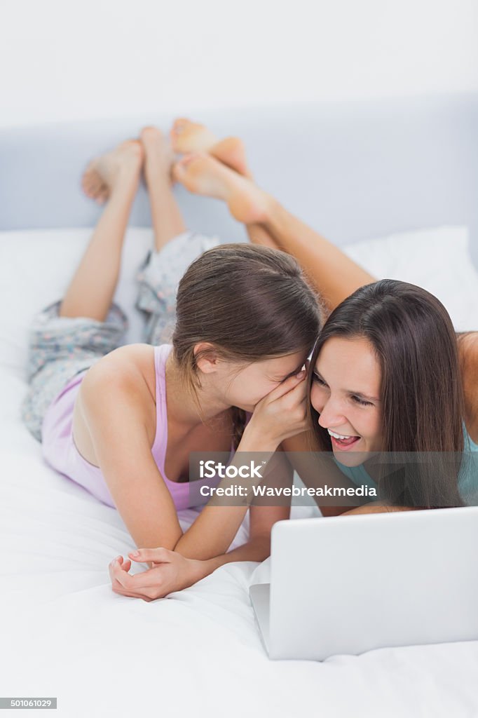 Friends lying in bed in pajamas with laptop Friends lying in bed in pajamas with laptop and telling secrets 20-29 Years Stock Photo