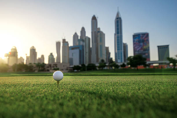 Playing golf at sunset. Golf ball is on the tee for a golf ball on the green grass of the golf course against the background the city skyscrapers at sunset