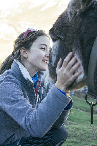 Woman smiling stroking the head of a donkey