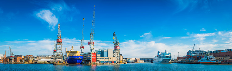 Helsinki, Finland - May 17, 2015: Big blue panoramic skies over the cargo cranes, shipyards and working docks reflecting in the tranquil waters of Helsinki harbour in the heart of Finland's vibrant capital city. Composite panoramic image created from eight contemporaneous sequential photographs.