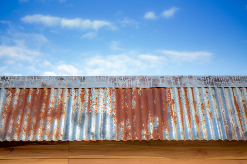 Old iron roof on teakwood house with blue sky and white clouds