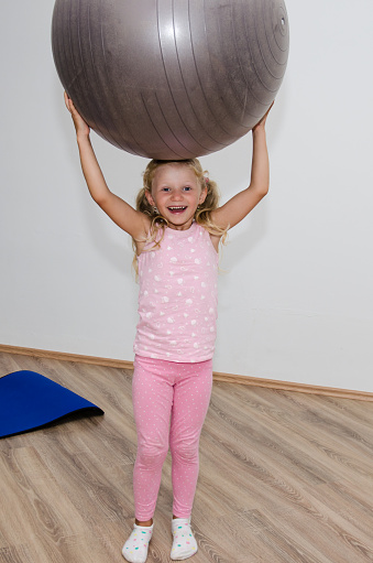 little blond girl holding gray fit ball over her head