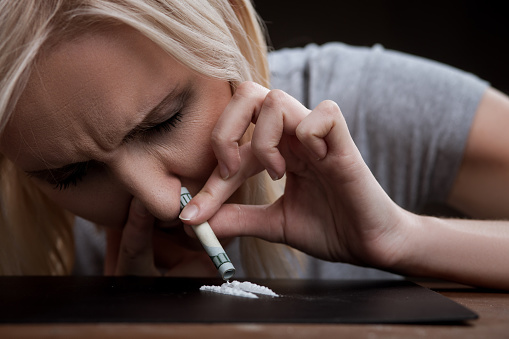 Close up of woman enhancing cocaine into her nose. She is sitting and closed her eyes with depression
