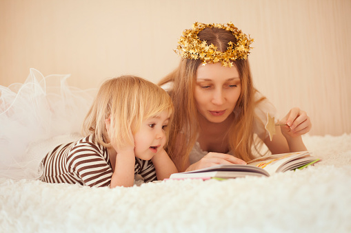 A cute small girl lying next to her mother while they are read a book. Having fun in imaginary land.
