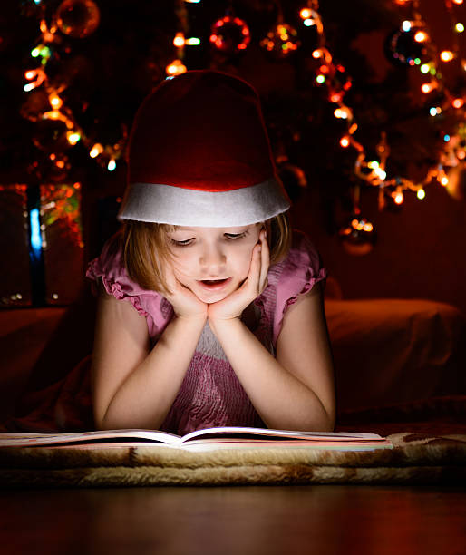 istock Little girl reading a book beside  Christmas tree 501097604