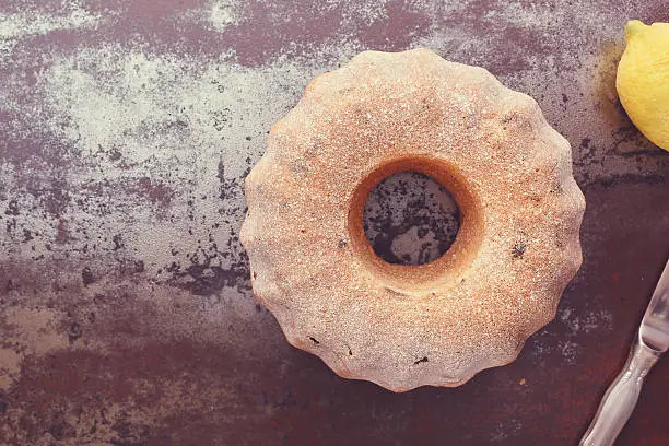 Homemade Bundt cake dusted with icing sugar on  rustic table.  Top view, blank space, vintage toned image